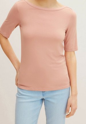 Kurzärmliges, figurbetontes Oberteil aus weichem Blush-Stoff mit einem Boot-Ausschnitt. Verfügt über eine glatte Textur und ein minimalistisches Design. Kombiniert mit hellblauen Jeans.