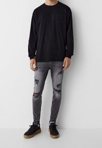 Black long-sleeve shirt with front pocket, gray distressed skinny jeans, and black sneakers with gum soles. Background is plain white.