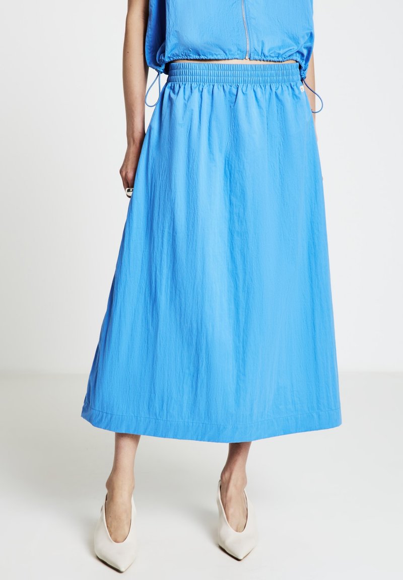 Jupe bleu clair mi-longue en tissu texturé avec une ceinture élastique. Associée à des escarpins blancs à bout pointu.