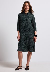 Abito camicia verde con stampa leopardata, dotato di una chiusura con bottoni davanti e maniche a tre quarti. Presenta una vestibilità comoda e un orlo di lunghezza media.