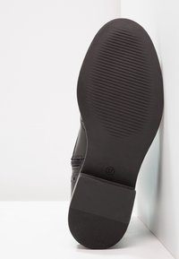 Suola di scarpa in pelle nera con una superficie piatta e testurizzata e linee orizzontali sollevate. Taglia 37 stampata sulla suola, a dimostrazione di durata e design.