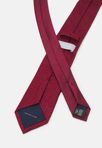 Cravat din mătase burgundă, cu un model texturat, vârf ascuțit și o etichetă din material albastru închis pe care este inscripționat "MICHAEL KORS."