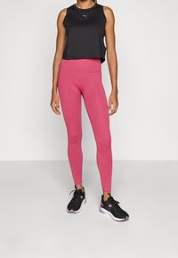 Czarny krótki top, różowe legginsy i czarne buty sportowe. Legginsy mają gładką teksturę i wysoką talię dla wsparcia.