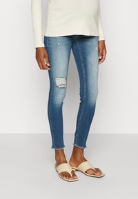 Bleka blå skinny jeans med ett slitaget på knäet och fransad fåll, tillsammans med beige slidesandaler. En långärmad ljus topp fulländar outfiten.