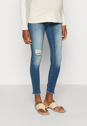 Falmede blå skinny jeans med et slitt kne og frynset kant, parret med beige slidersandaler. En langermet lys topp fullfører antrekket.