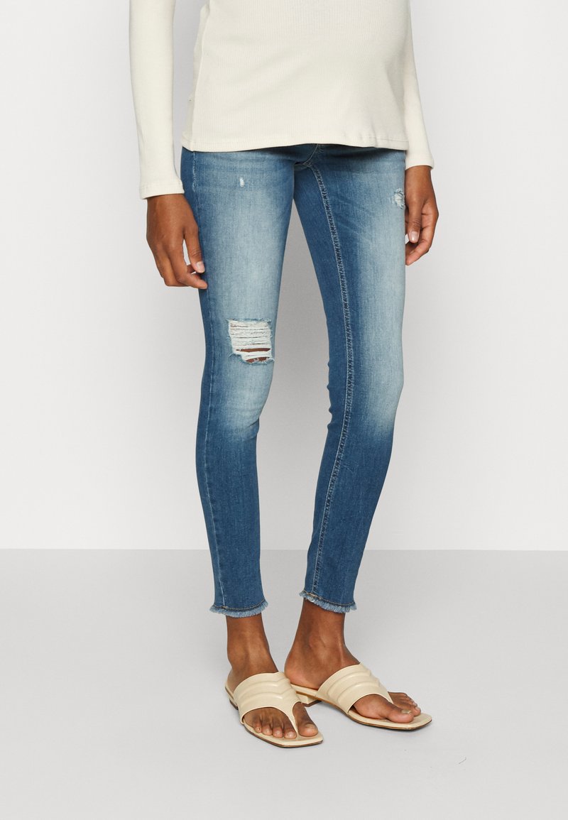 Bleka blå skinny jeans med ett slitaget på knäet och fransad fåll, tillsammans med beige slidesandaler. En långärmad ljus topp fulländar outfiten.