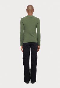 Pull vert côtelé à manches longues avec une coupe ajustée ; assorti à un pantalon cargo noir taille haute avec poches latérales et coupe droite.