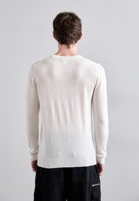 Helles Cremefarbenes, langärmliges Strickoberteil mit geripptem Halsausschnitt und Saum, das eine glatte Textur und einen subtilen Farbverlauf auf der Rückseite aufweist.