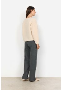 Ljust beige textured fleece-tröja med långa ärmar, tillsammans med mörkgrå vida byxor. Mjuka material och avslappnad silhuett.