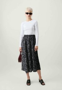 Biely top s dlhými rukávmi v kombinácii s čiernou sukňou s bielymi abstraktnými vzormi, čiernymi otvorenými mules topánkami a malou bordó kabelkou.