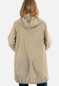 Chubasquero beige con capucha, material ligero, dobladillo elástico y textura suave. Presenta un diseño minimalista y mangas largas.