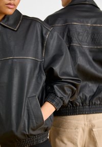 Svart läderbomberjacka med krage, ribbade ärmslut och elastisk nederkant. Har en slät textur och framfickor.