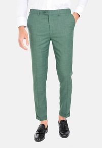 Pantaloni verdi a fantasia con una vestibilità slim, realizzati in tessuto testurizzato. Presentano una chiusura a bottone e tasche laterali, abbinati a scarpe nere.