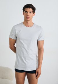 Light gray short-sleeve t-shirt made of smooth cotton material, featuring a classic round neck and a regular fit, paired with black shorts.