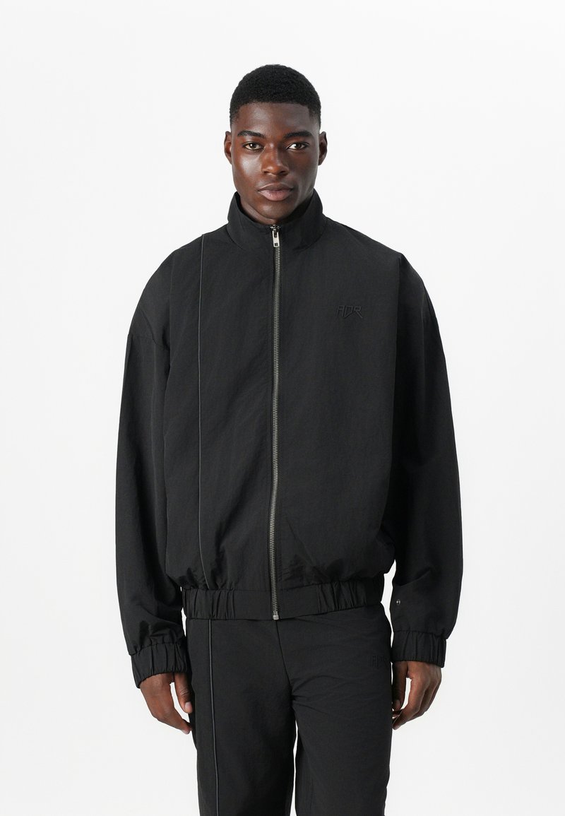 Schwarze Bomberjacke mit Reißverschluss, Stehkragen, elastischen Bündchen und Saum. Sie verfügt über einen strukturierten Stoff und ein minimales Logodesign auf der Brust.
