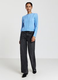Helles blaues Strickpullover mit strukturierten Mustern und einem gerippten Saum, kombiniert mit hoch sitzenden, schwarzen Weitlegjeans und schwarzen Ankle Boots.
