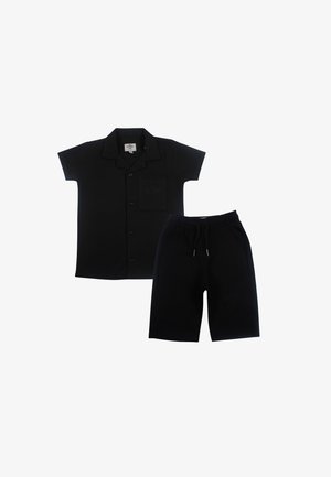 Chemise noire à manches courtes avec boutons, col et poche poitrine associée à un short noir à cordon à hauteur du genou.