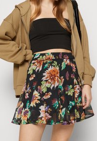 Jupe fleurie avec un fond noir, ornée de fleurs colorées en orange, vert et violet. Taille élastique ; matériau léger et fluide.