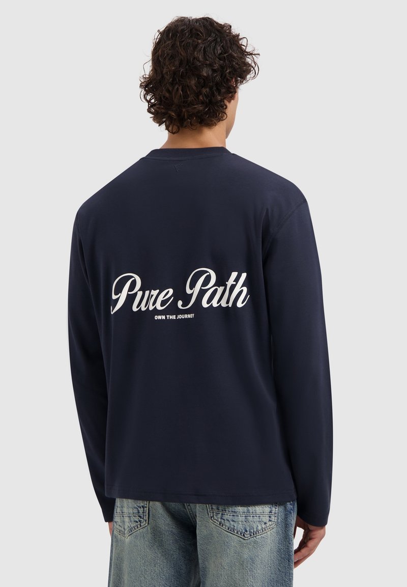 Marineblauwe lange mouwen shirt met een ronde halslijn, voorzien van witte tekst op de achterkant die luidt "Pure Path" en "Own the Journey." Gemaakt van katoen.