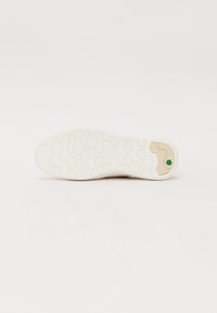 Sola de ténis brancos com um padrão hexagonal, com um detalhe em castanho e verde, feita de borracha para tração e durabilidade.
