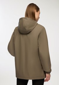 Giacca impermeabile leggera color verde oliva con cappuccio, vestibilità rilassata, polsini elasticizzati e texture liscia e opaca. Adatta per l'uso all'aperto.