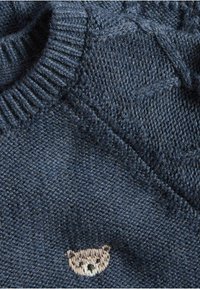 Tummansininen neulepusero, jossa on ribatty kaula-aukko ja tekstuuriset kuviot; siinä on pieni vaaleanruskea brodeerattu karhumoottivi.