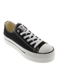 Zapatilla de lona negra con puntera de goma blanca, acentos en negro y blanco, y cordones blancos. Presenta un diseño cosido y un logo en la lengüeta.