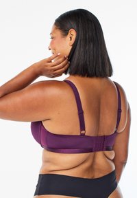 Paarse beha met verstelbare schouderbanden, zachte stof en gestructureerde achterkant. Beschikt over drie rijen haken voor maatverstellingen. Zwarte slip eronder.