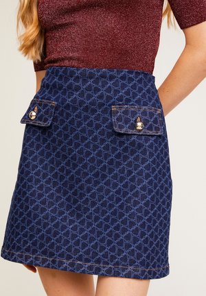 Spódnica dżinsowa w granatowym kolorze z geometrycznym wzorem na całej powierzchni, posiadająca dwa zewnętrzne kieszenie na klapę z metalowymi guzikami oraz widoczne przeszycia jako akcenty.