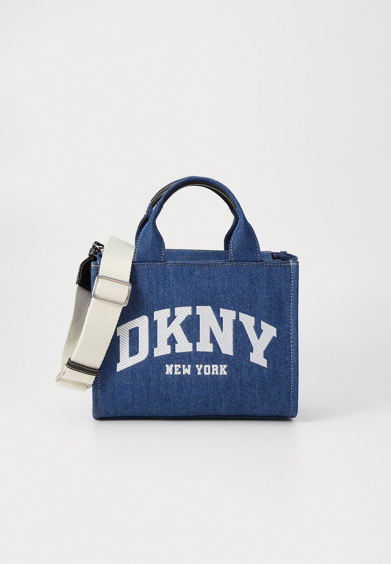 Sac en denim avec le logo blanc 'DKNY NEW YORK' et des coutures contrastantes. Dispose de courtes poignées et d'une bandoulière crème réglable. Forme rectangulaire.