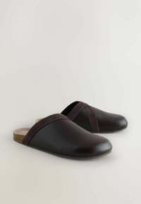 Zuecos de cuero marrón oscuro con una banda de ante sobre la parte superior. Textura suave, punta redondeada, diseño trasero abierto. Suela plana con detalles sutiles.