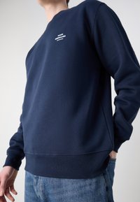 Σκούφος ναυτικού τύπου από ύφασμα με βαμβακερή σύνθεση, διαθέτει στρογγυλή λαιμόκοψη, ραμμένα μανίκια και μικρό λευκό λογότυπο στο στήθος.