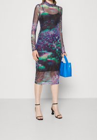 Robe longue à manches longs en voile avec un imprimé numérique multicolore dans les tons de violet et de vert. Associée à un sac à main structuré bleu vif et des talons noirs.