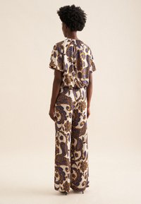 Completo a due pezzi con un motivo paisley floreale nei toni crema, viola e marrone. Top morbido e pantaloni larghi, realizzati in un tessuto leggero.