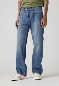 Blå denimbukser med lige pasform, mellemhøj talje, fem lommer og en subtil falmet finish, stylet med hvide sneakers.