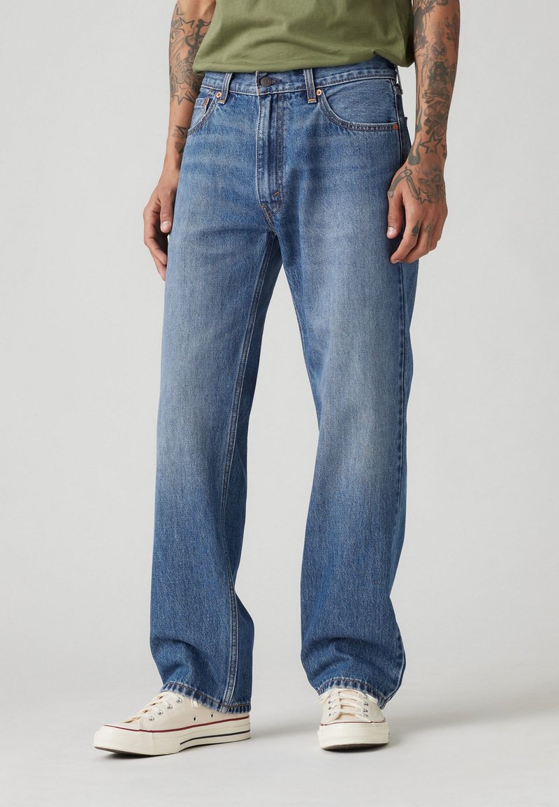 Blå denimbukser med lige pasform, mellemhøj talje, fem lommer og en subtil falmet finish, stylet med hvide sneakers.