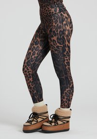 Leggings con stampa leopardata in marrone e nero con vita alta, abbinati a stivali beige con foderatura in pelliccia e lacci neri.