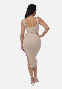 Abito midi a coste, beige, con schiena scolpita e spacco laterale. Presenta spalline sottili e una silhouette aderente, abbinato a scarpe con tacco a blocco trasparenti.