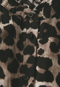 Halenka s leopardím vzorem v béžové a černé barvě s černými knoflíky. Má zapínání na knoflíky vpředu a texturovanou, lehkou tkaninu.