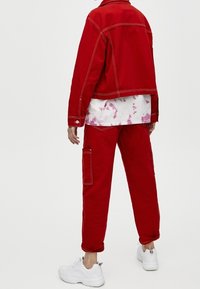 Red denim jacket and matching pants with white accents, worn with a tie-dye shirt, paired with white sneakers. Visible stitching details.