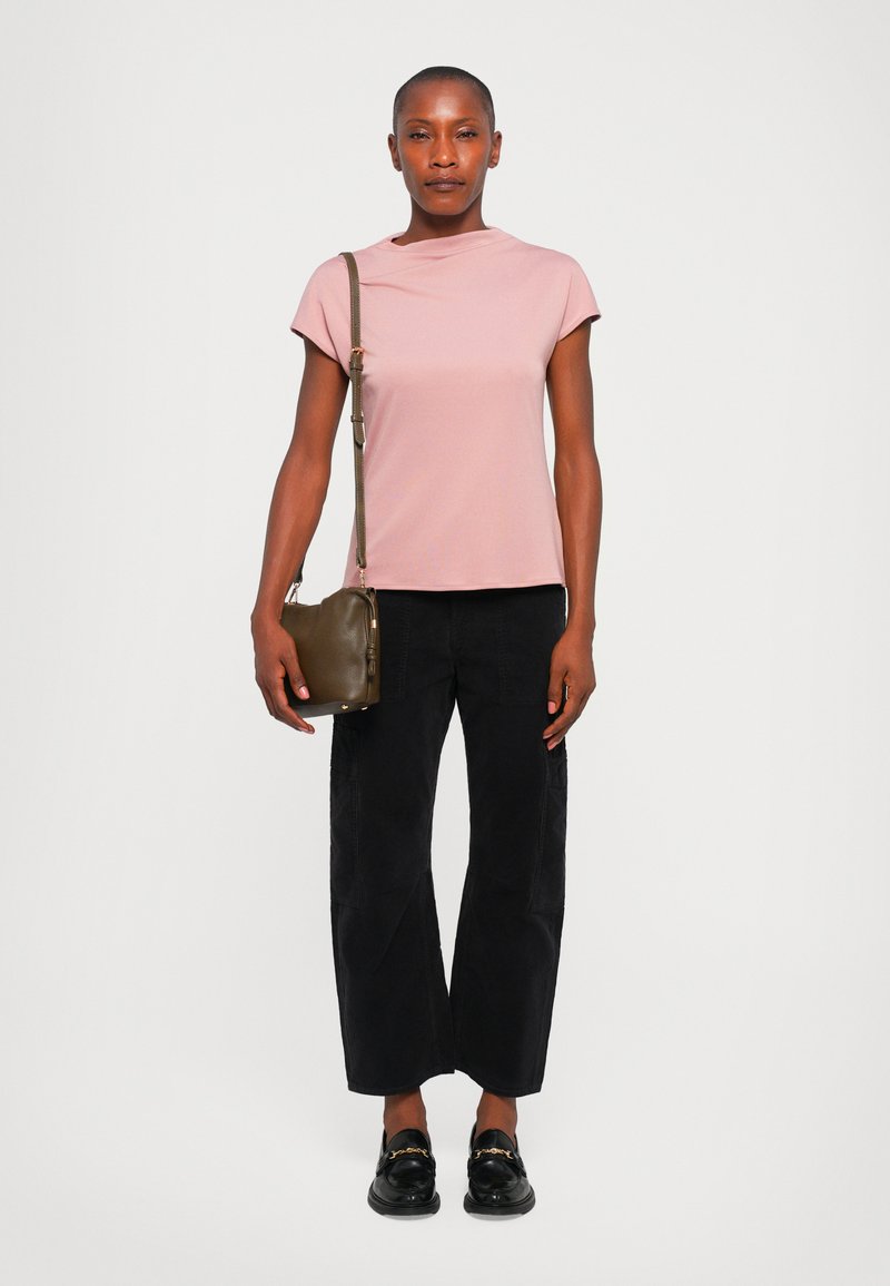 Haut rose clair à manches courtes, pantalon noir à jambes larges, mocassins noirs et petit sac bandoulière vert olive. Design simple, texture lisse.