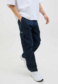 Marinblå cargobyxor i bomullsblandning, med flera sidofickor, avslappnad passform och kombinerade med vita träningsskor.