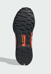 Schwarze Gummi-Sneaker-Sohle mit tiefen, kantigen Profilmustern. Mit einem roten Akzent und dem "Continental"-Logo in Orange in der Mitte.