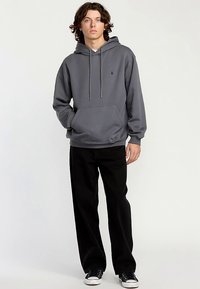 Sweat à capuche gris avec poche avant et cordon de serrage, associé à un pantalon noir à jambes larges et des baskets noires. Texture lisse et coupe décontractée.