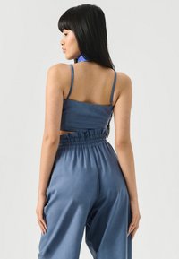 Denim dviejų dalių komplektas, kuriame yranutrumpintas švarkas su plonomis petnešomis ir aukštu liemeniu laisvi džinsai, pagaminti iš minkštos mėlynos medžiagos.