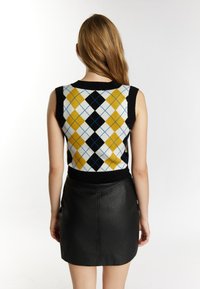 Top senza maniche in maglia con bordi neri, caratterizzato da un motivo argyle multicolore in giallo, blu e bianco. Abbinato a una gonna in pelle nera.