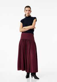 Top de manga corta en color marino combinado con una falda maxi burdeos que presenta una cintura fruncida, tela texturizada y botas negras de tobillo con punta.