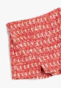 Tejido de tweed en rojo y crema con un patrón texturizado, que presenta una ligera abertura en el dobladillo y un acabado suave y tejido.