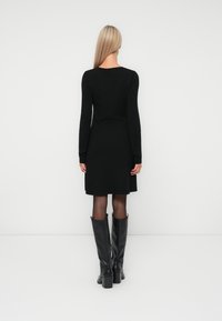 Robe noire à manches longues avec un corps ajusté et un ourlet évasé, associée à des bottes noires montantes avec un large talon et une texture lisse.