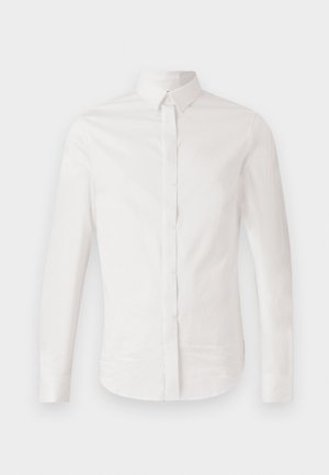 Camicia bianca a maniche lunghe in cotone morbido, con colletto classico, chiusura con bottoni sul davanti e orlo curvo, impreziosita da un discreto dettaglio del logo ricamato.